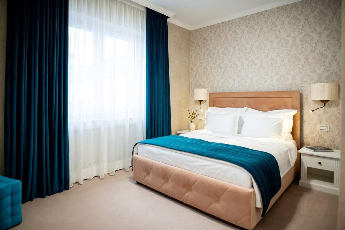 A hotel room with a large bed, a nightstand, a lamp, and a window with curtains.