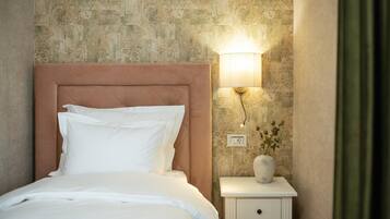 Uma cama bem arrumada com roupa de cama branca, cabeceira, mesa de cabeceira com abajur e um vaso com flores.