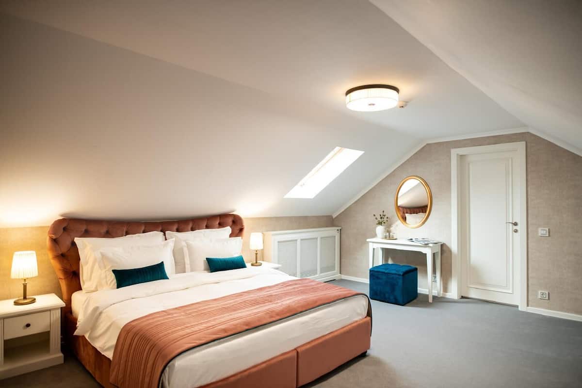 A bedroom with a large bed, a desk, a mirror, and a skylight.