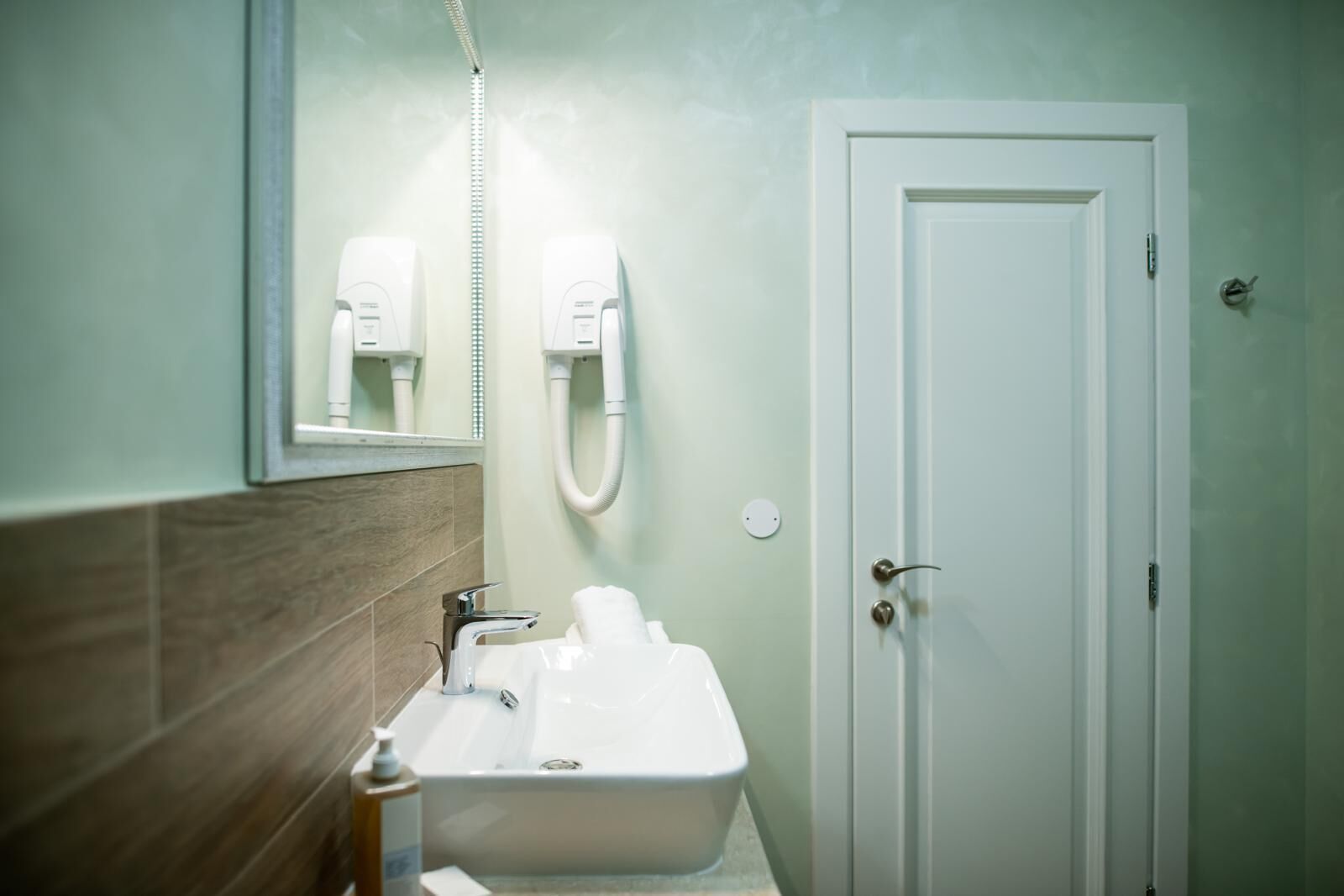 A bathroom with a white sink, a mirror, a towel dispenser, and a door.