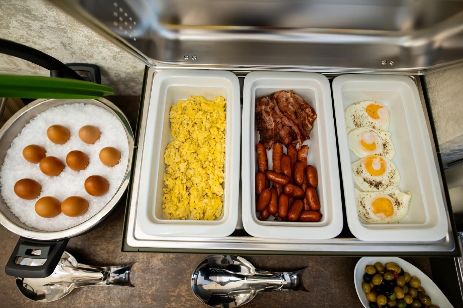 A breakfast buffet with scrambled eggs, sausages, and bacon.