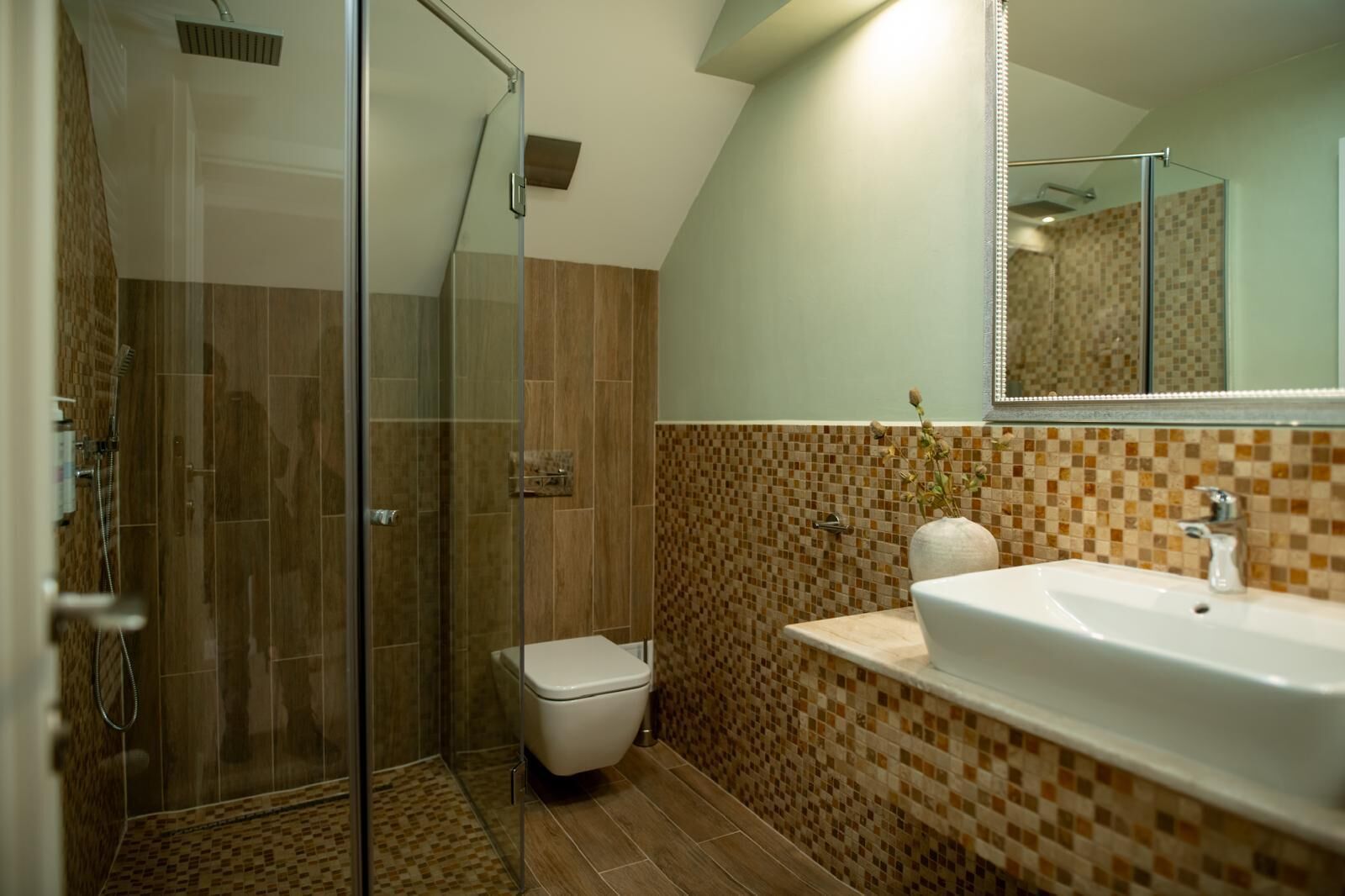 Un baño moderno con mampara de vidrio, inodoro blanco y lavamanos con salpicadero de mosaico.