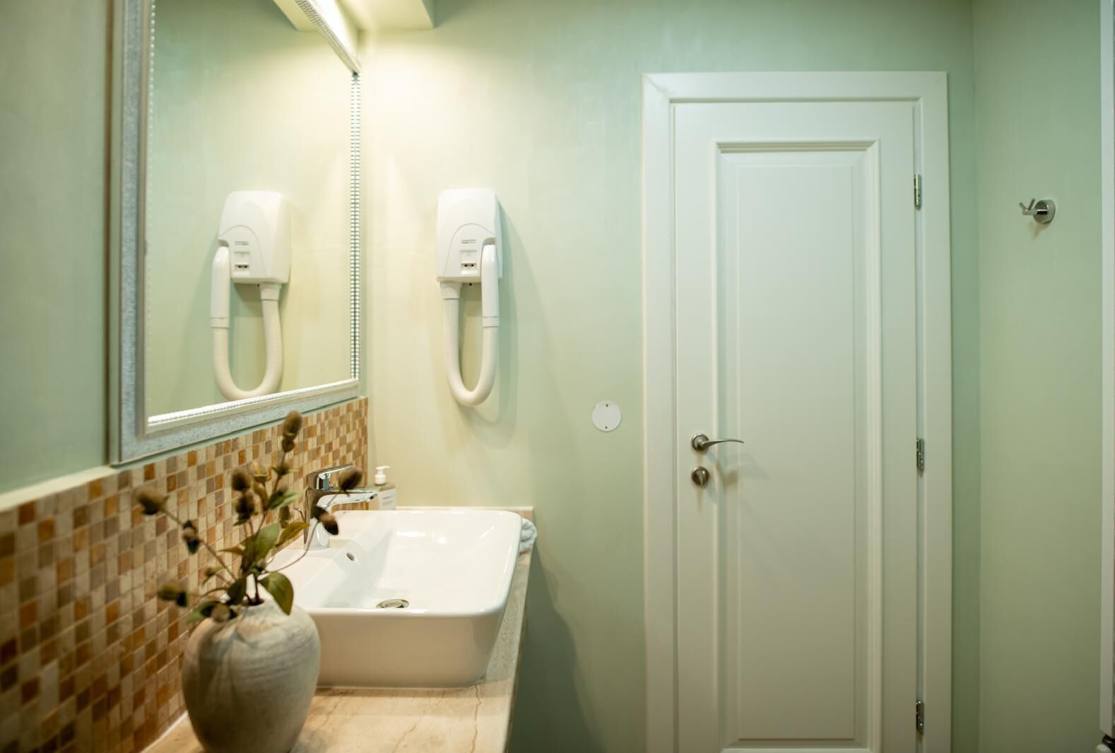 Un baño con un lavamanos blanco, un espejo y una puerta.