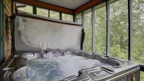 Una vasca idromassaggio con un pontile in legno e vista sugli alberi attraverso ampie finestre.