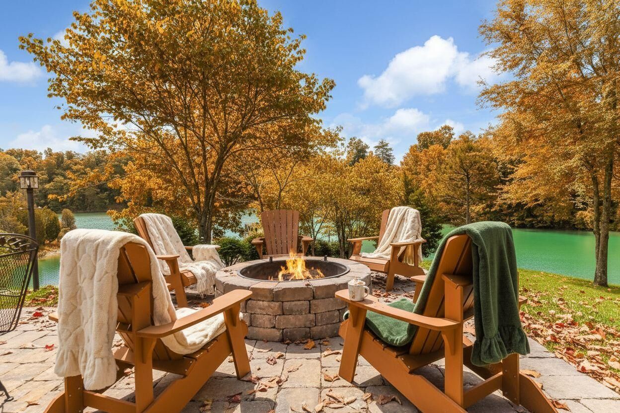 Ein Lagerfeuer, umringt von Adirondack-Stühlen mit Decken, auf einer Steinterrasse mit Blick auf einen See und Herbstlaub.