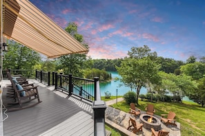 A deck with rocking chairs and a fire pit overlooking a lake.