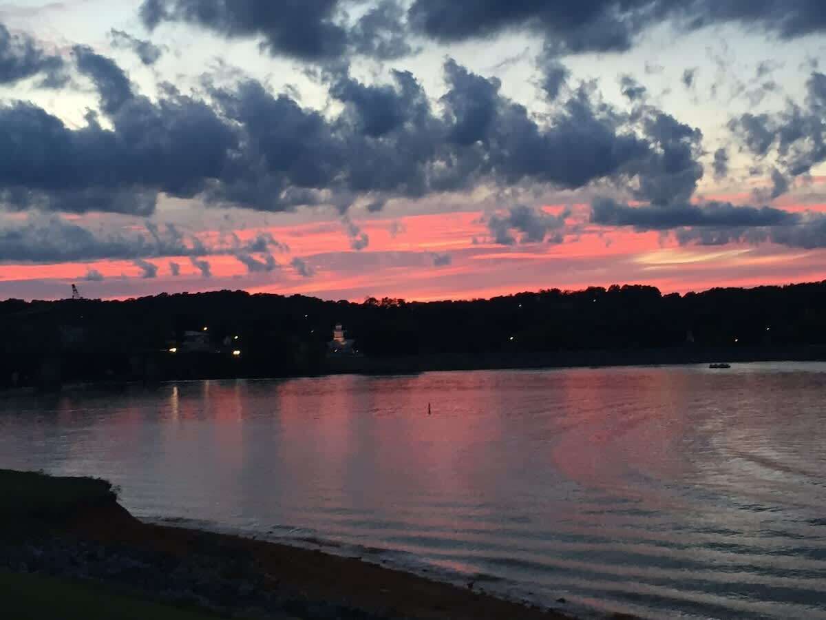Sunset over a calm lake with silhouetted hills and scattered clouds