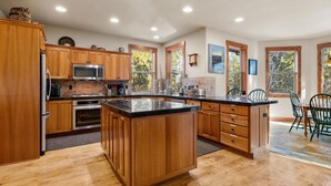 A spacious kitchen with wooden cabinets, a central island, and large windows offering views of trees. - Hot Tub Home Near Phil's Trail Sleeps 8 Pets OK (Bend)