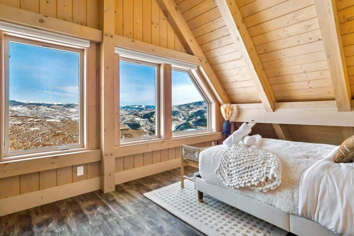 Une chambre avec un plafond en bois et de grandes fenêtres donnant sur un paysage montagneux.
