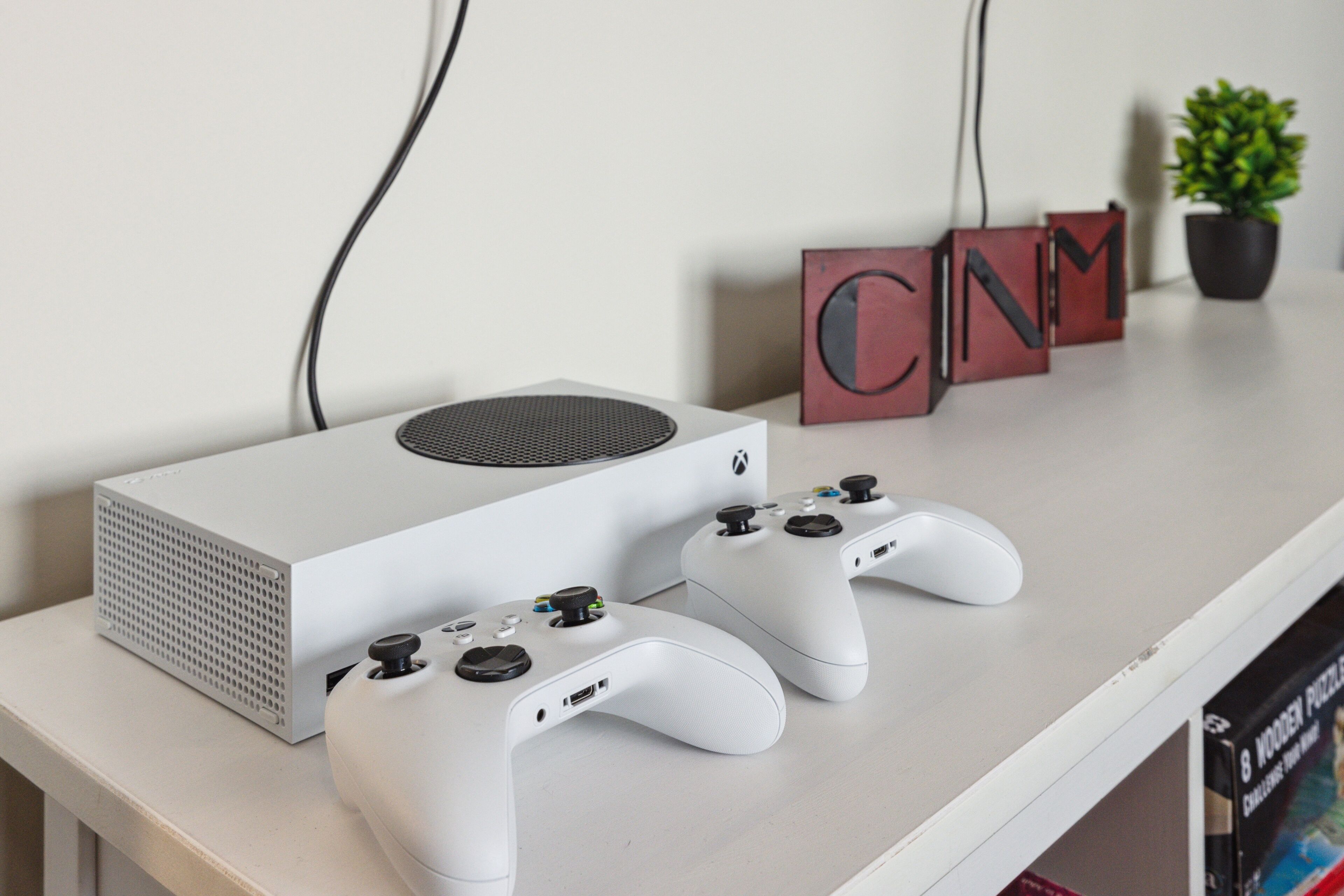 Un ensemble de jeu comprenant une console Xbox blanche, deux manettes blanches et un panneau rouge avec le sigle « CNN » placé sur une table blanche.