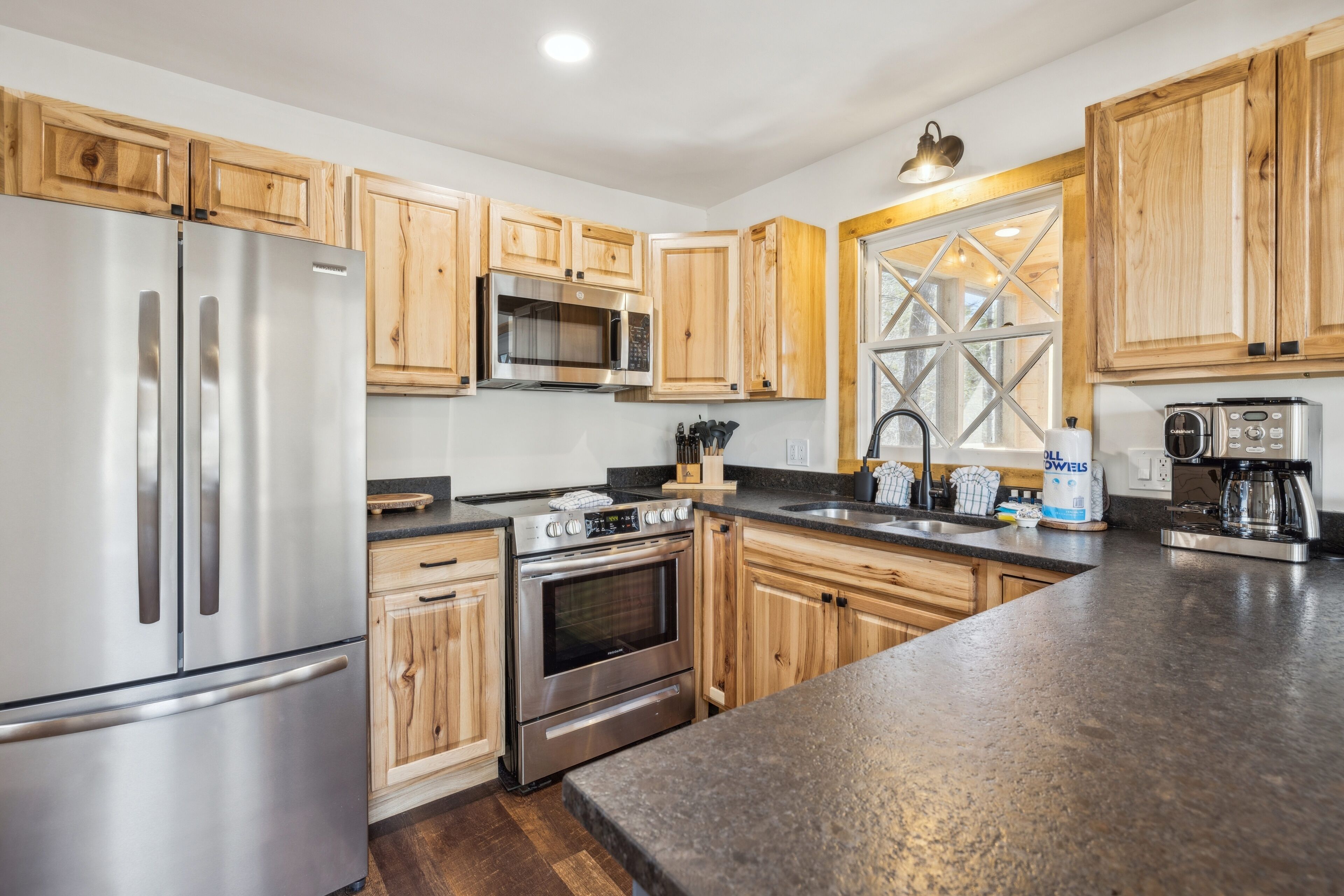 A kitchen with wooden cabinets, stainless steel appliances, a large window, and a granite countertop.
