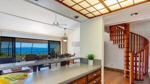 A modern kitchen with a large island, wooden cabinets, and a view of the ocean. - Maalaea Surf C10 2 Bedroom Condo (Kihei)