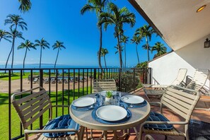 A round table set for four with plates, glasses, and cutlery, overlooking a beach with palm trees and a clear blue sky. - Maalaea Surf C10 2 Bedroom Condo (Kihei)