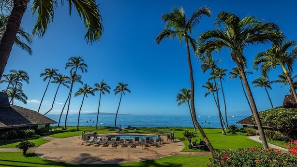 A pool area with lounge chairs, surrounded by palm trees and a view of the ocean. - Maalaea Surf C10 2 Bedroom Condo (Kihei)