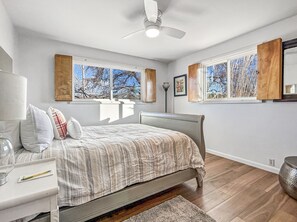 A bedroom with a bed, bedside table, lamp, windows, and a ceiling fan. - Retro Retreat A 60's Time Capsule 3 Bedroom Home (Grand Junction)