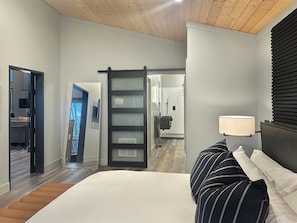 A bedroom with a bed, a nightstand, a lamp, and a view of a bathroom. - Mountain-Modern couples retreat in Bryson City with hot tub, fireplace, king bed free train tix (Bryson City)