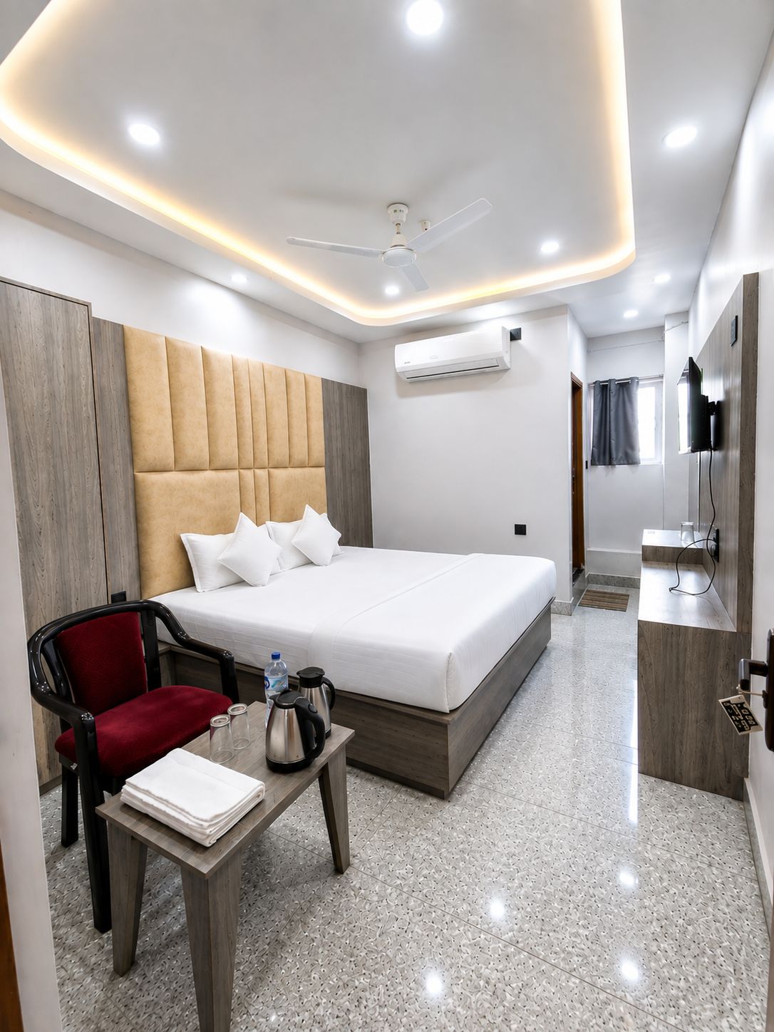 Una habitación de hotel moderna con una cama grande, una silla roja, una mesita con un hervidor de agua y un equipo de aire acondicionado.