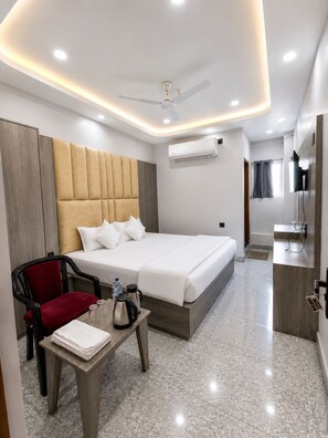 A modern hotel room with a bed, a desk, a chair, an air conditioning unit, and a television. - Hotel Ganesha (Muzaffarpur)