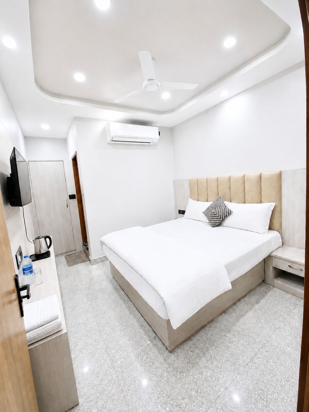 Camera d'albergo con letto, comodino, TV a schermo piatto, condizionatore d'aria e ventilatore a soffitto.