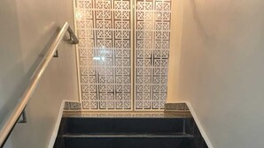 Una scala con gradini neri e un corrimano in metallo, che conduce a un muro con un pannello decorativo.