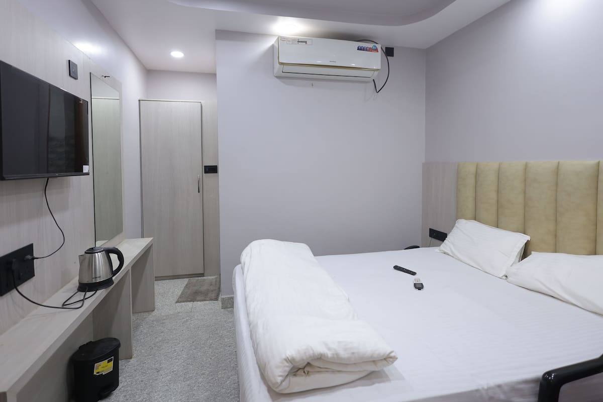 A hotel room with a bed, bedside table, TV, air conditioning unit, and a door.