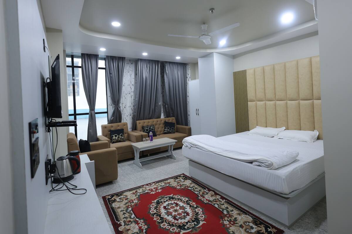 A modern hotel room with a bed, sofa, coffee table, and a TV.