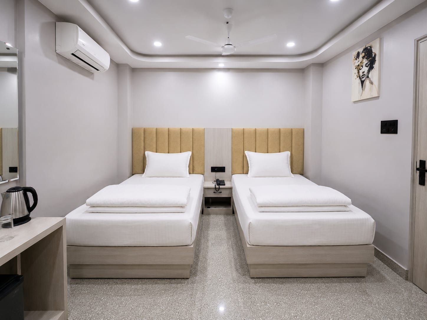 Habitación de hotel con dos camas, un escritorio, cafetera, aire acondicionado, ventilador de techo y un cuadro en la pared.