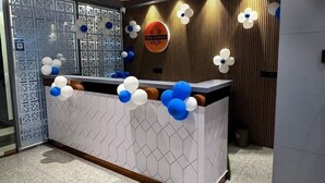 Un'area reception dal design moderno, con un bancone a motivi geometrici, illuminazione decorativa e un logo sulla parete.