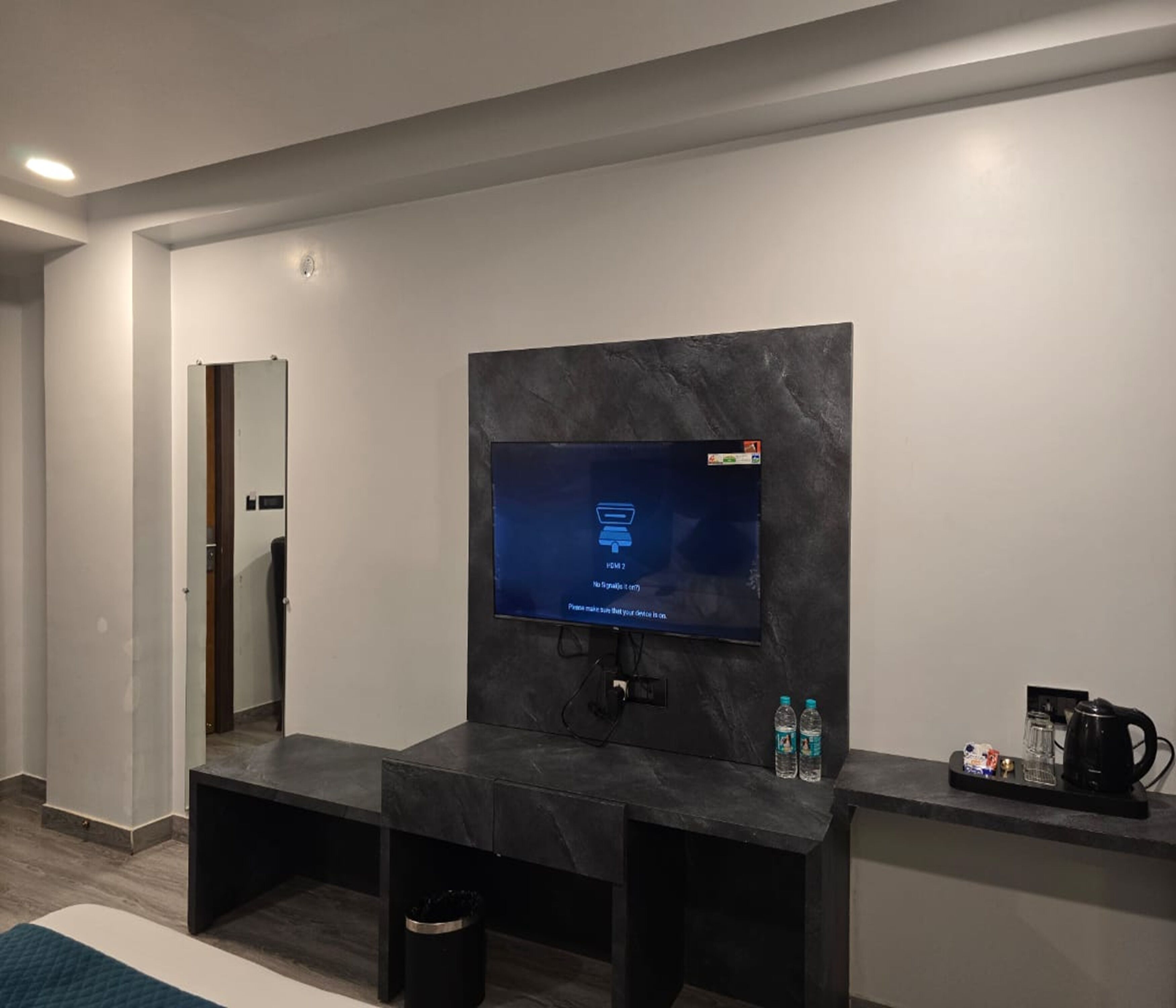 A modern living room with a flat-screen TV mounted on a dark marble wall, a built-in bench, and a coffee maker on a small table.