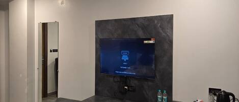 A modern living room with a flat-screen TV mounted on a dark marble wall, a built-in bench, and a coffee maker on a small table.