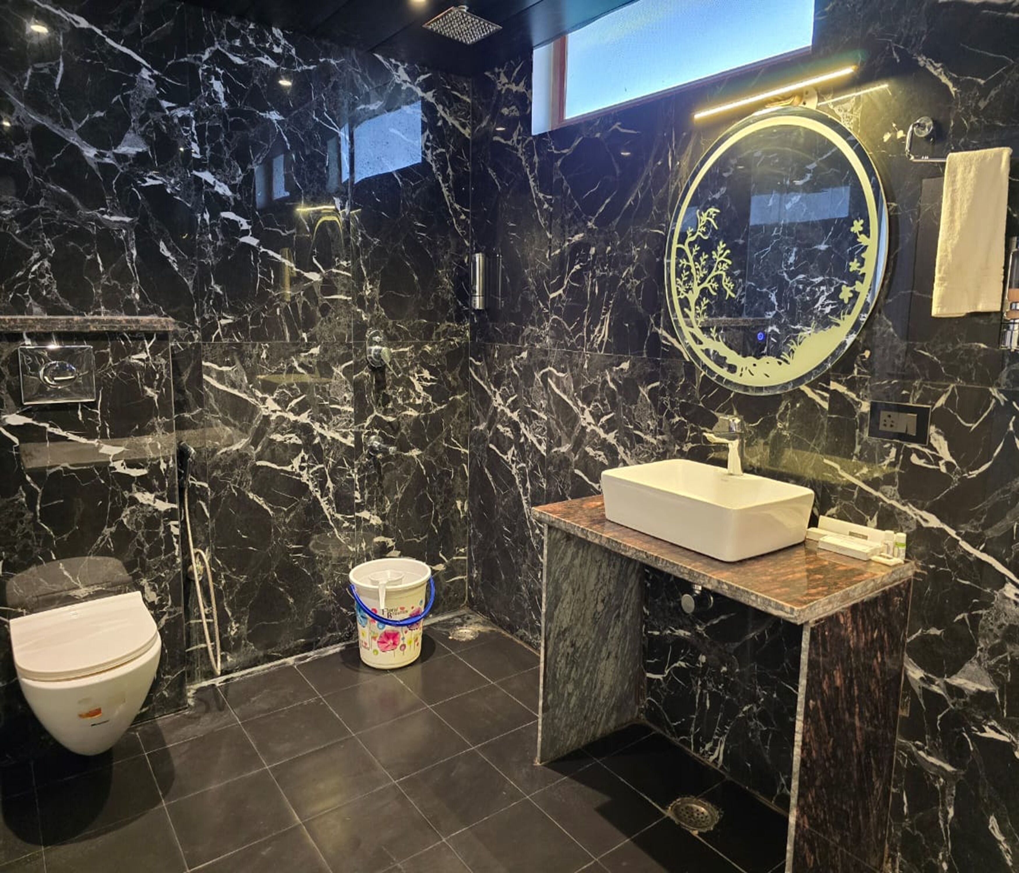 A modern bathroom with a marble wall, a round mirror, a rectangular sink, and a toilet.