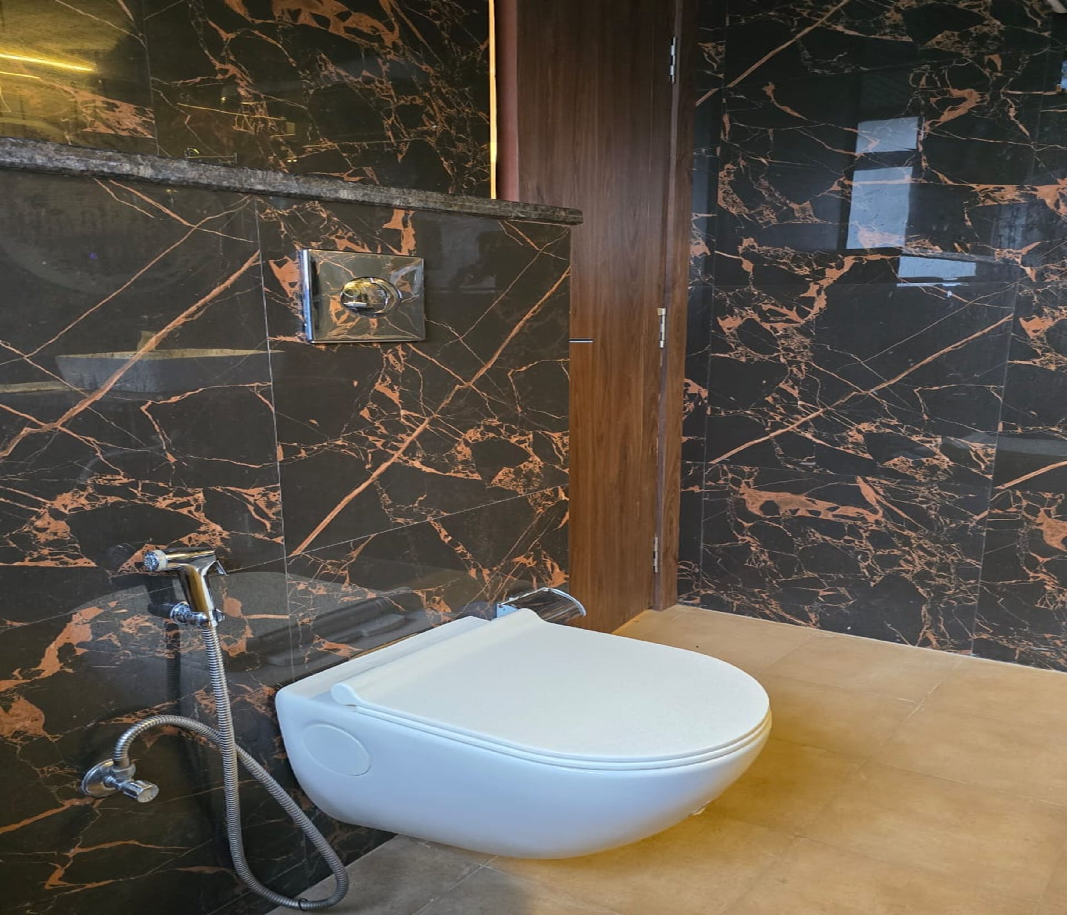 A bathroom with a white toilet, a shower with a handheld hose, and a marble wall with a gold pattern.