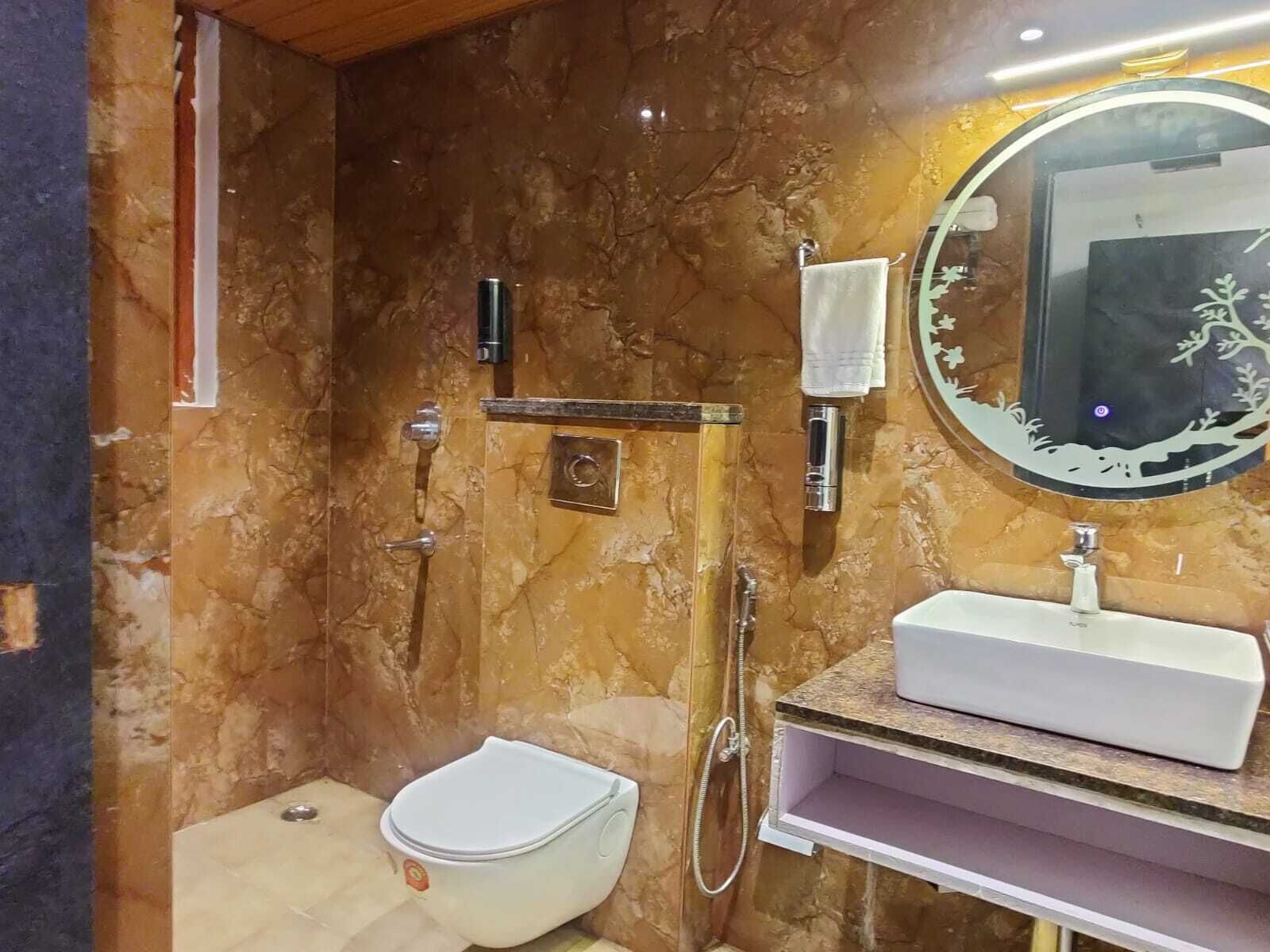A bathroom with a marble wall, a white sink, a toilet, and a shower area with a handheld showerhead.