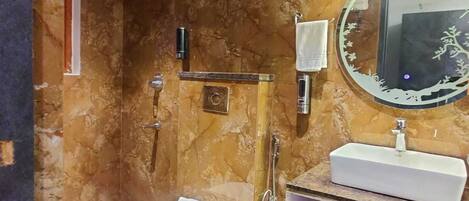 A bathroom with a marble wall, a white sink, a toilet, and a shower area with a handheld showerhead.
