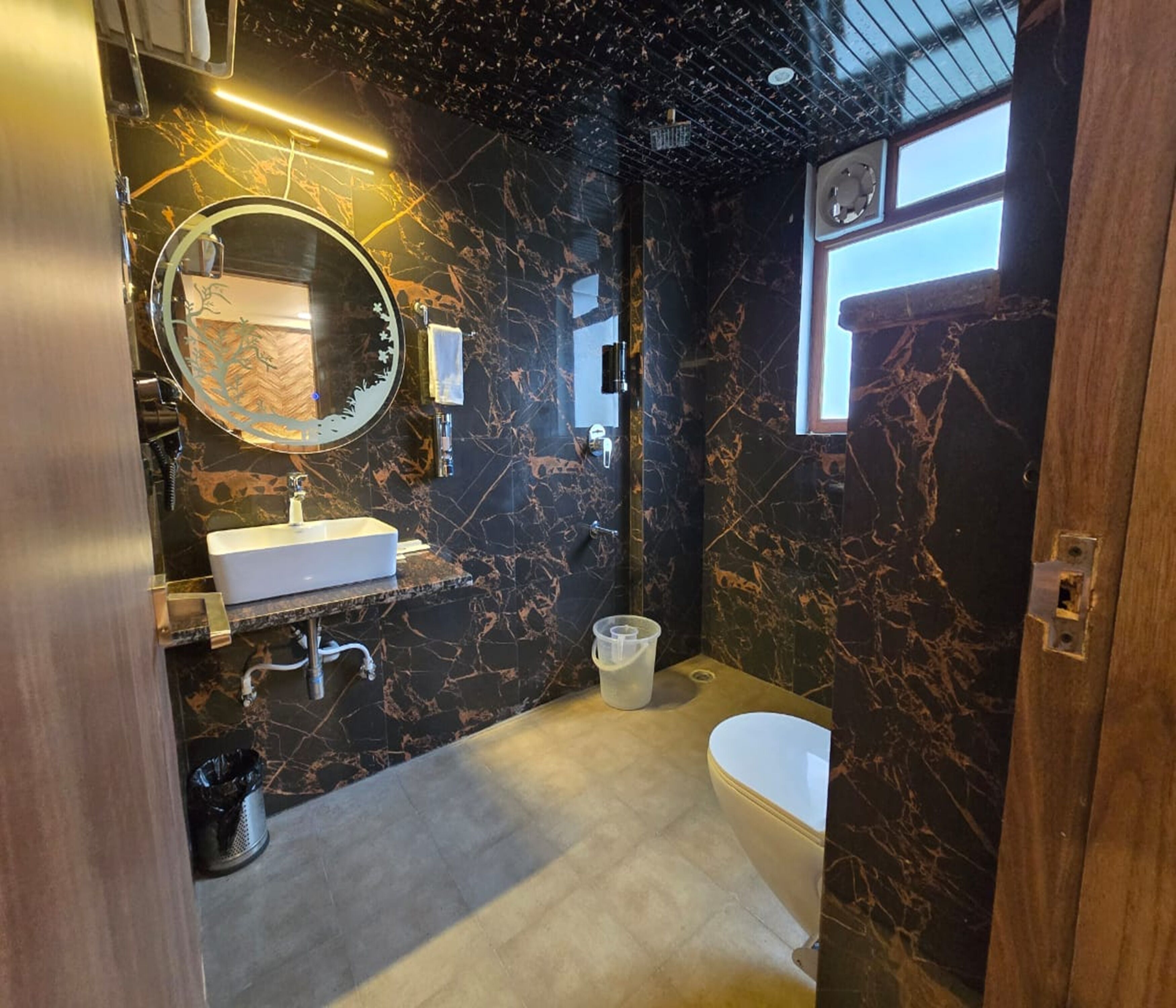 A modern bathroom with a marble wall, a round mirror, a white sink, a toilet, and a bathtub.