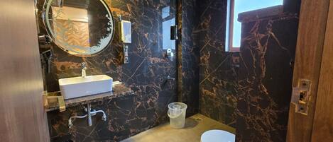 A modern bathroom with a marble wall, a round mirror, a white sink, a toilet, and a bathtub.