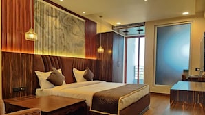 A modern hotel room with a large bed, wooden paneling, a desk, and a view of the outdoors. - Hotel KHS Landmark Prayagraj - The Boutique Hotel (Prayagraj)