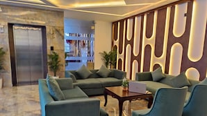 A modern lobby with a sectional sofa, armchairs, a coffee table, and a laptop on it. There is a decorative wall with vertical lighting and a bookshelf in the background. - Hotel KHS Landmark Prayagraj - The Boutique Hotel (Prayagraj)