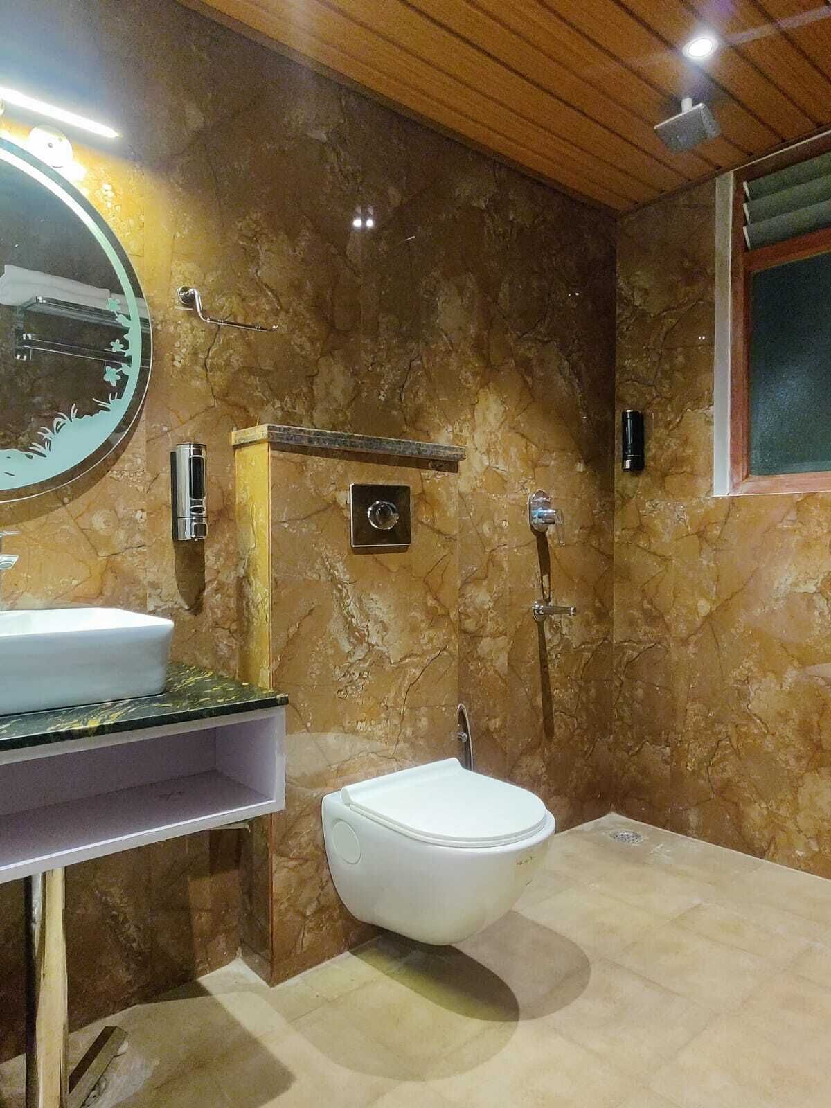 Un baño con pared de mármol, un lavamanos blanco, un espejo redondo y un inodoro.