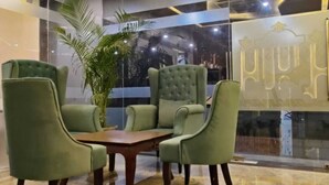 A lobby with a marble floor, green upholstered chairs, a wooden coffee table, and a large potted plant. - Hotel KHS Landmark Prayagraj - The Boutique Hotel (Prayagraj)