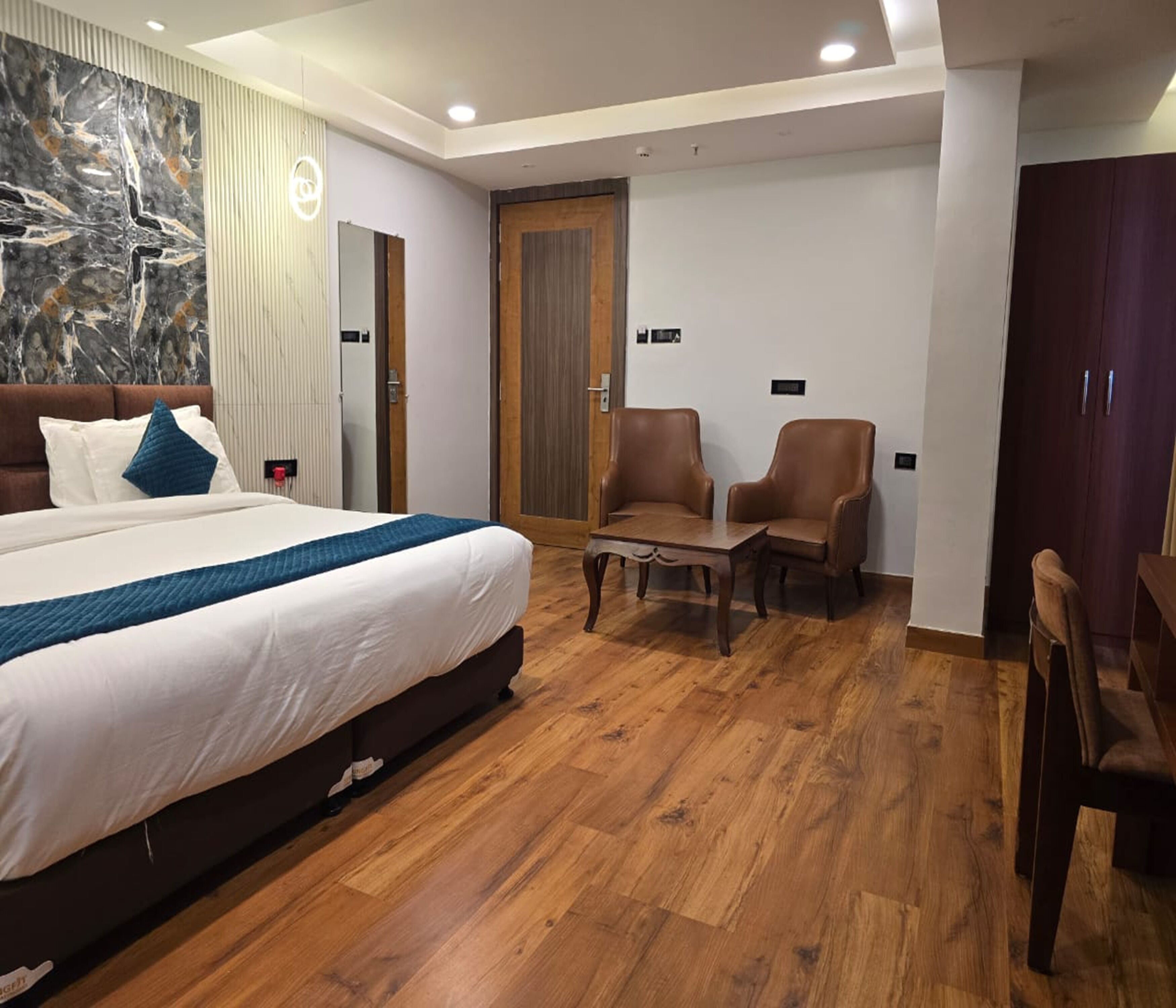 A hotel room with a large bed, two armchairs, a small table, and a wooden floor.