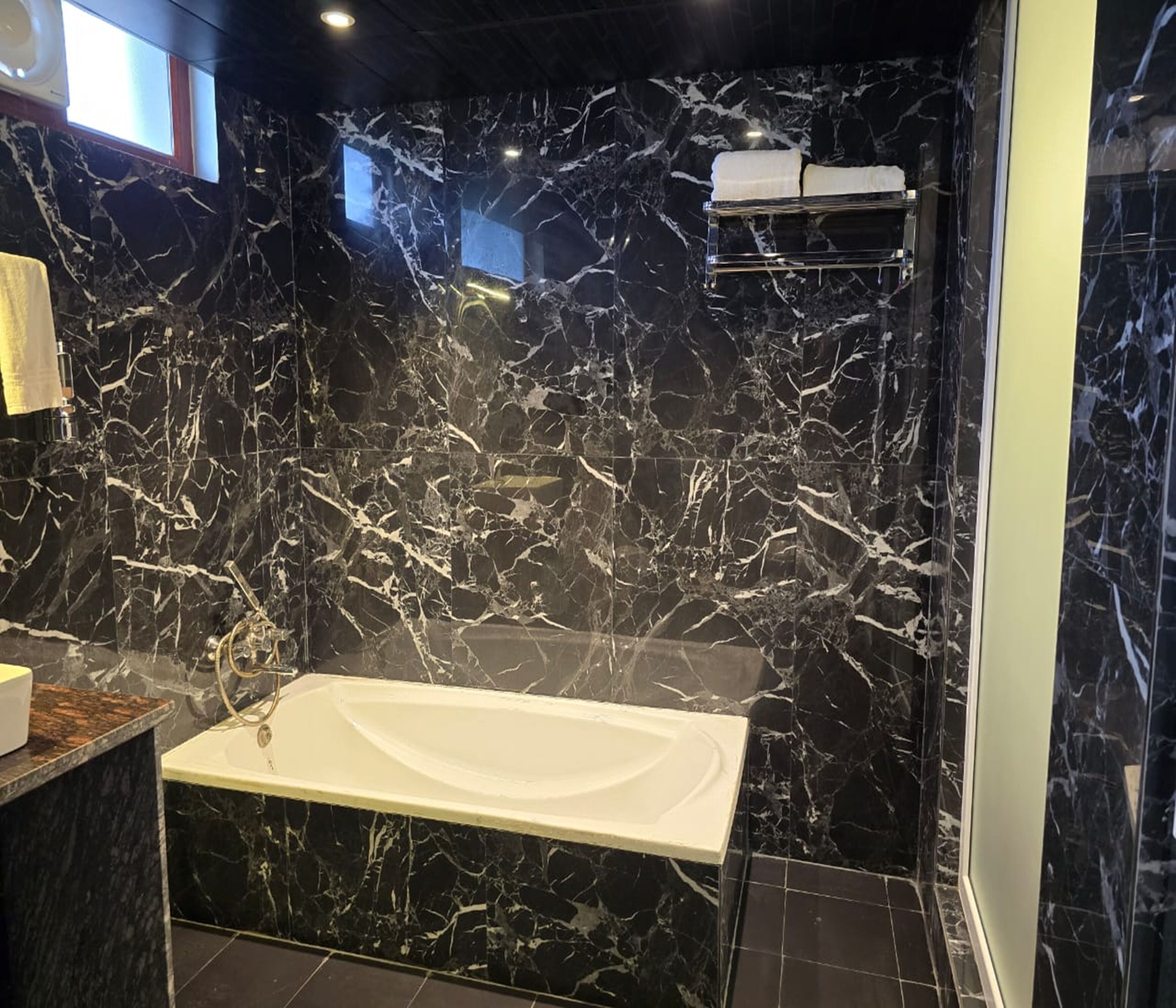 Un bagno con una parete in marmo, una vasca da bagno bianca e un porta asciugamani.