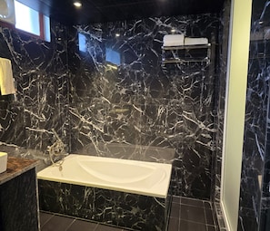 A bathroom with a marble wall, a white bathtub, and a towel rack. - Hotel KHS Landmark Prayagraj - The Boutique Hotel (Prayagraj)