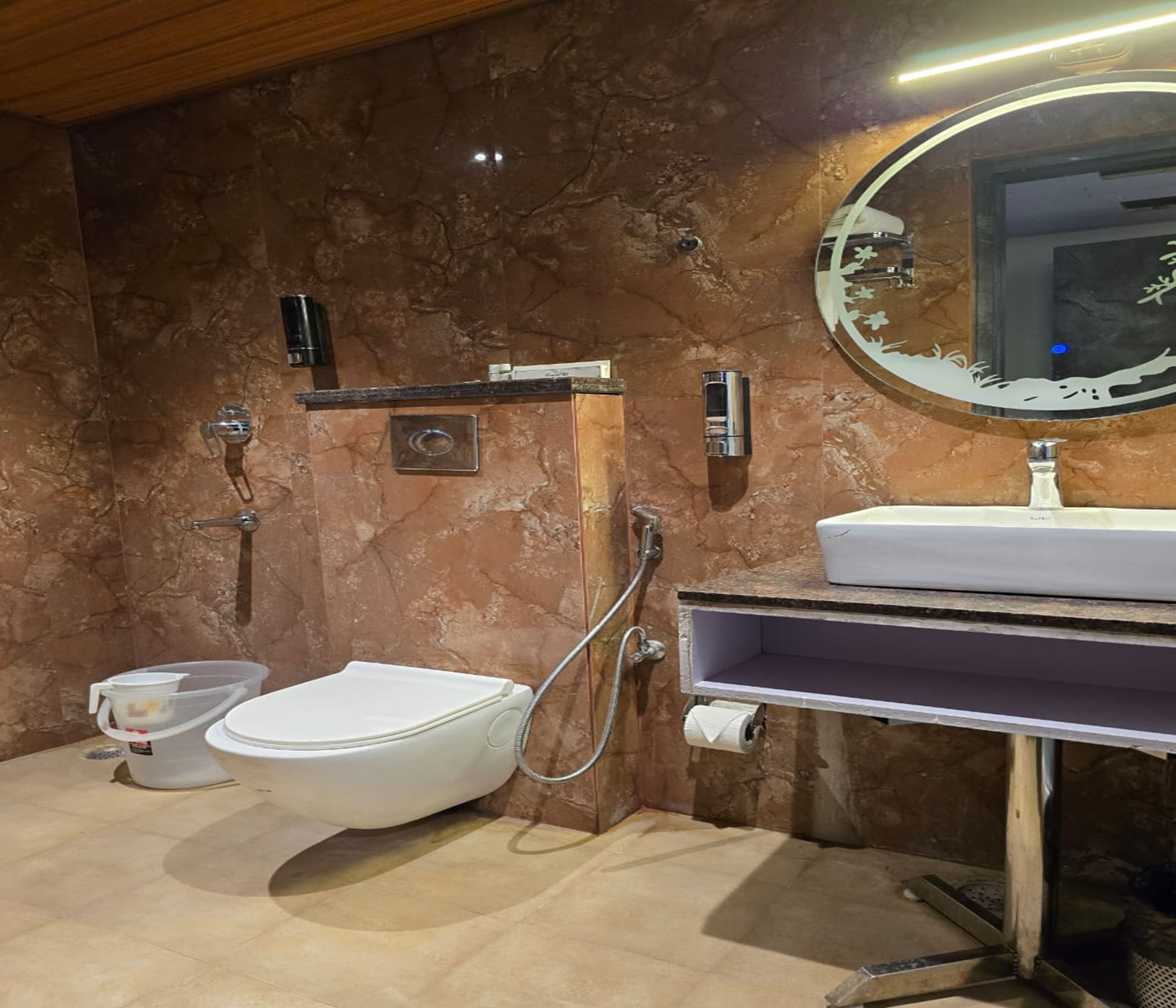 Un baño con pared de mármol, inodoro, bidé, lavamanos y espejo.