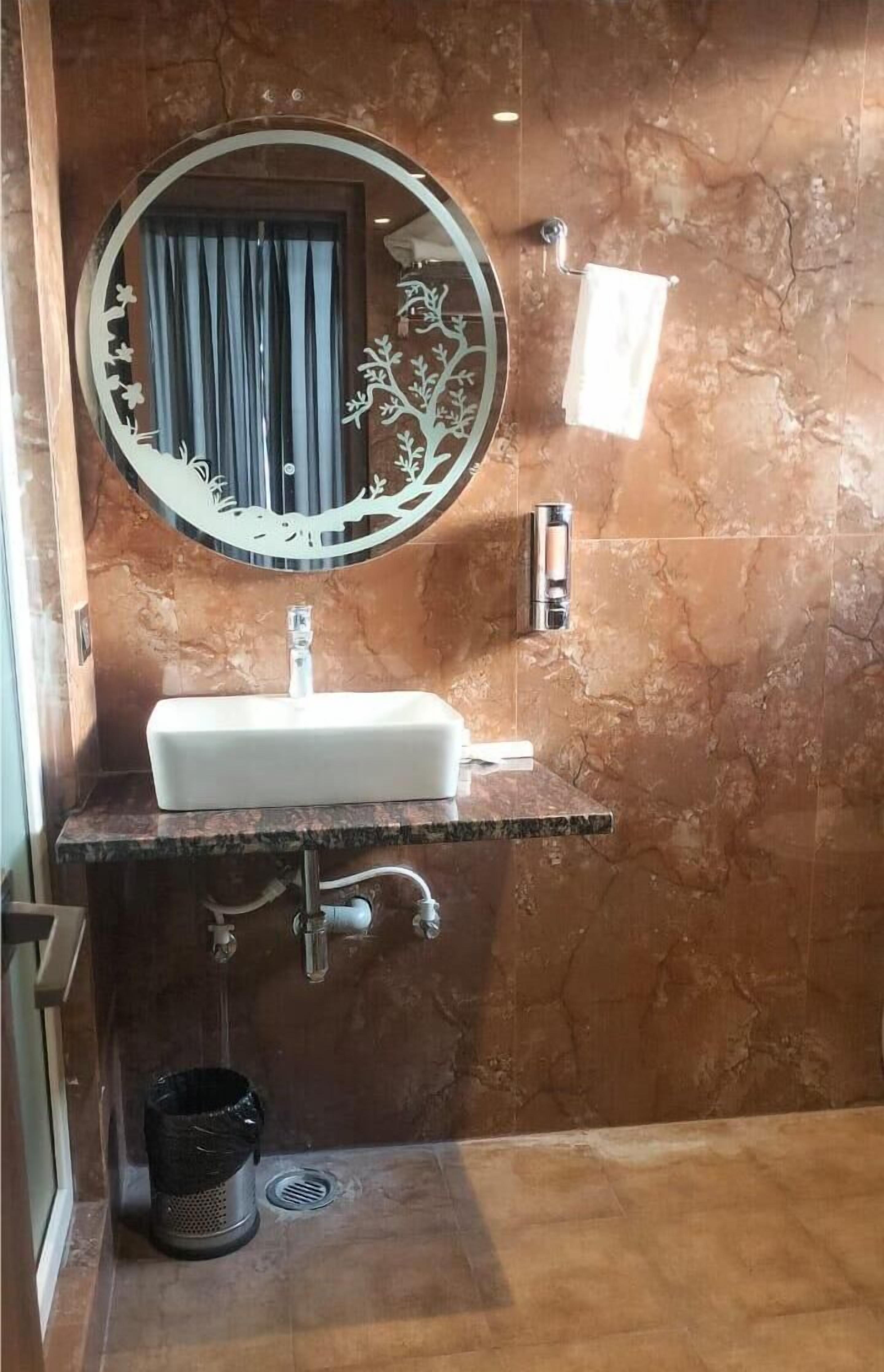 Ein Badezimmer mit einem weißen Waschbecken, einem runden Spiegel mit Baumdekor und einem Handtuchhalter.