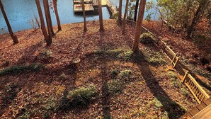 Vista de un lago con un muelle y una zona de estar cubierta, rodeado de árboles y hojas secas.