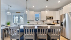 Una cocina moderna con armarios blancos, electrodomésticos de acero inoxidable y una isla central con taburetes de bar.