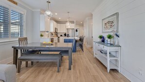 Una cocina moderna con armarios blancos, un comedor con banco, y una mesita auxiliar con objetos decorativos.