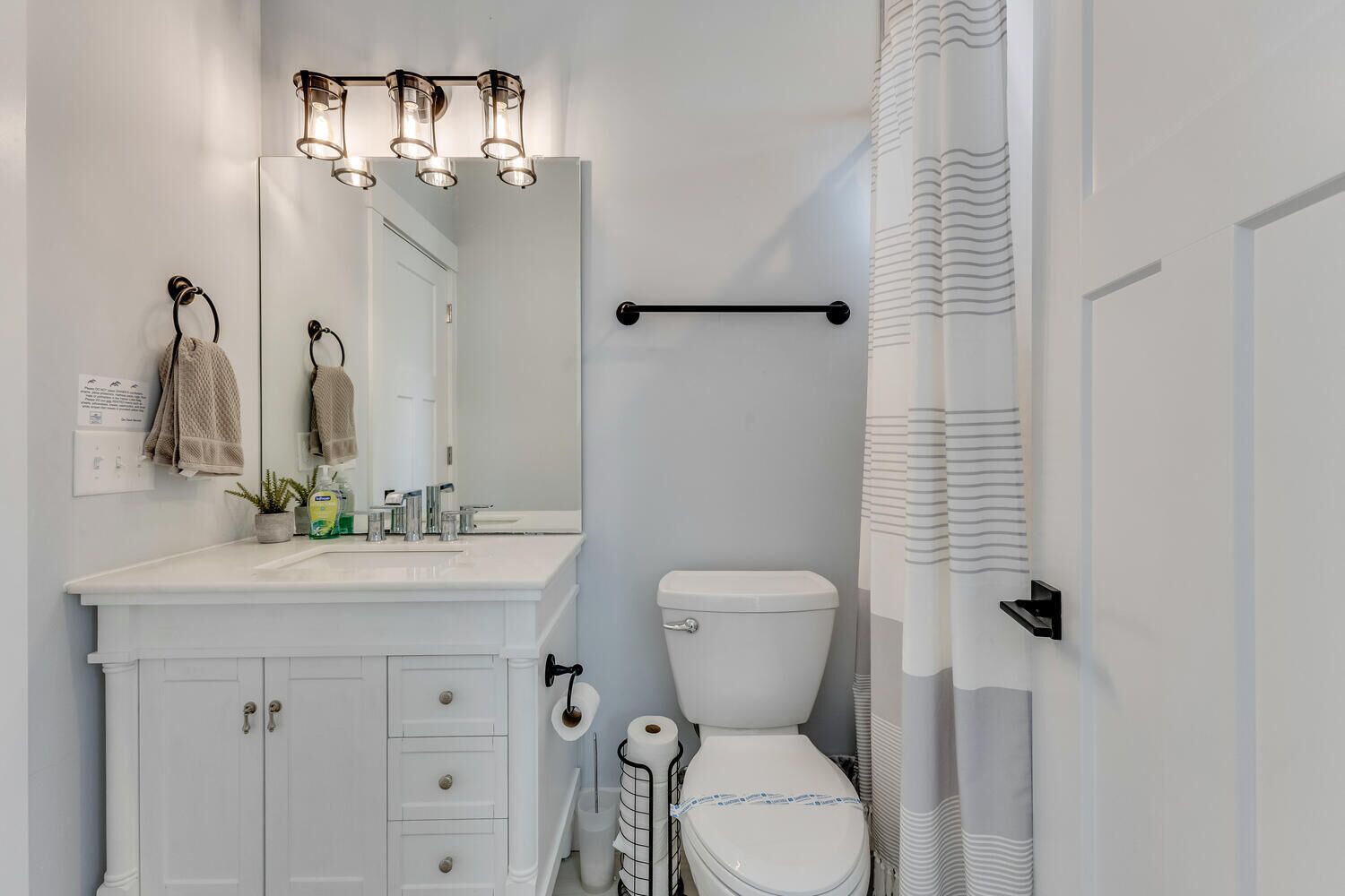 A modern bathroom with a white vanity, a large mirror, a toilet, and a shower curtain.