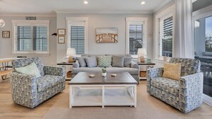 Un salon moderne comprenant un canapé, deux fauteuils à motifs, une table basse et une grande fenêtre avec des stores.